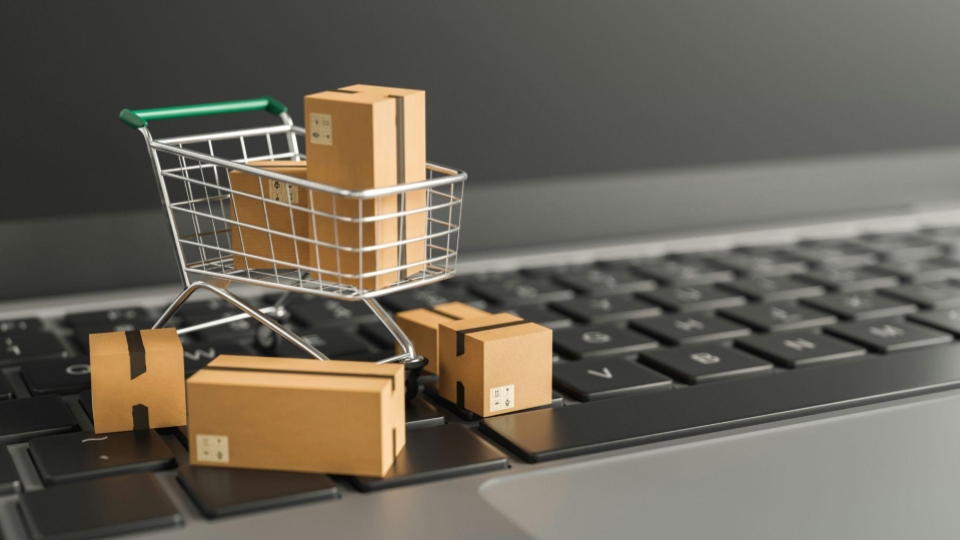 Miniatura de carrinho de compras e pequenas caixas de papelão sobre o teclado de um notebook, simbolizando e-commerce.