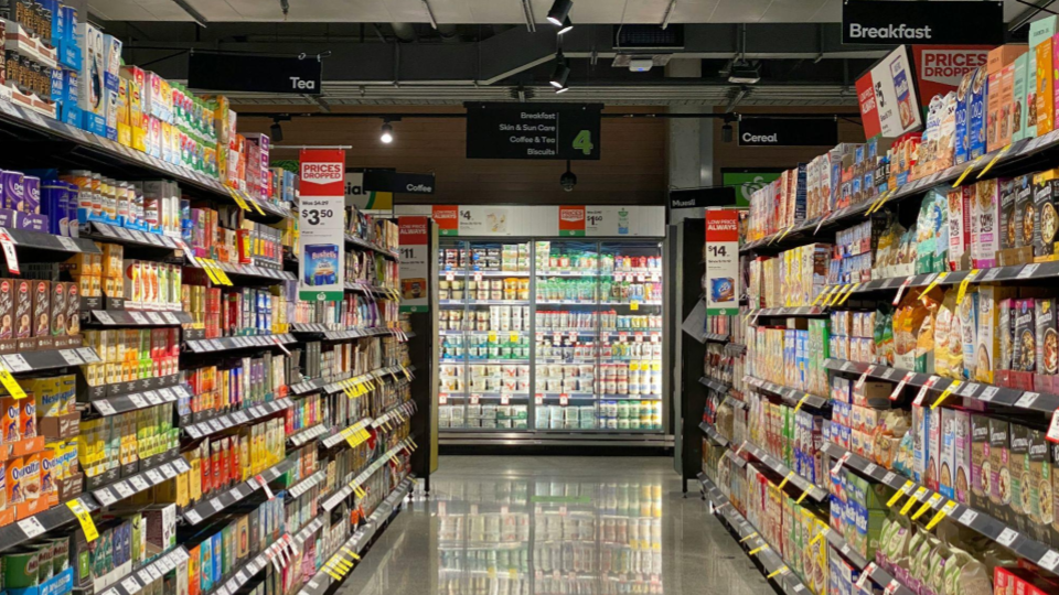 Tubulações e trilhos expostos com iluminação focada nos produtos. O ambiente transmite eficiência operacional e modernidade funcional.